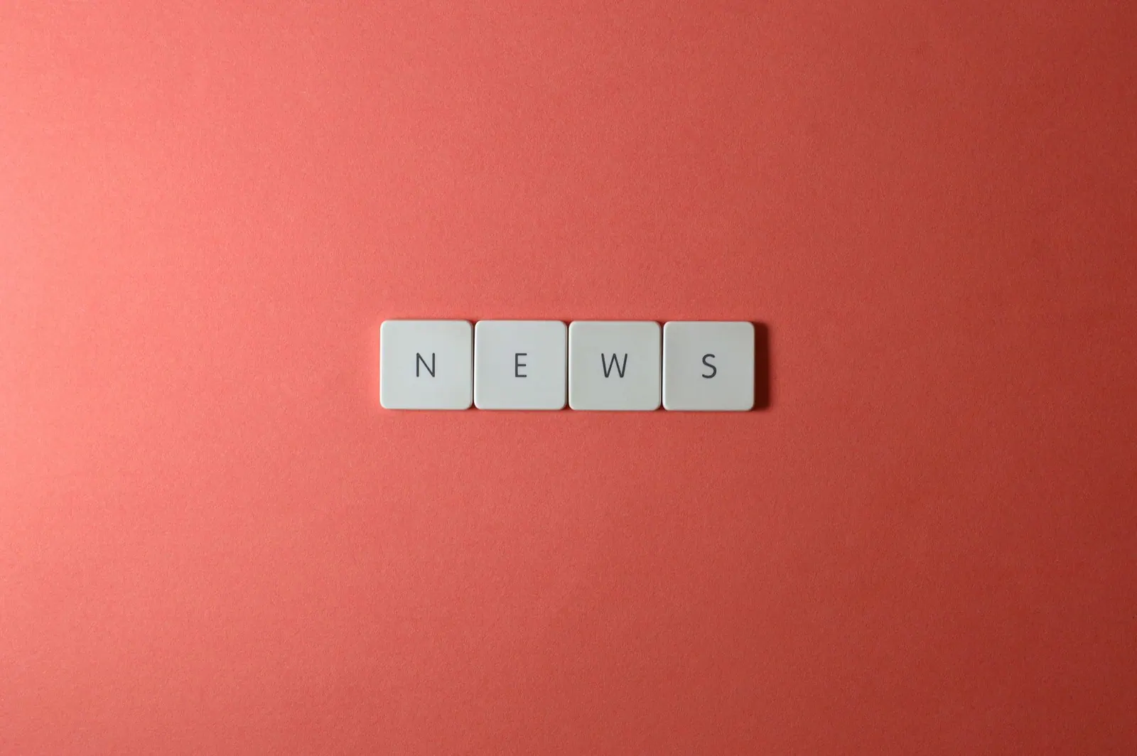 Close-up of keyboard keys spelling 'NEWS' on a red background, minimalist style.