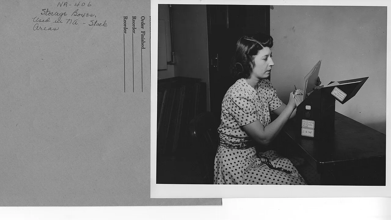 An archival photograph showing storage boxes and a worker reviewing records